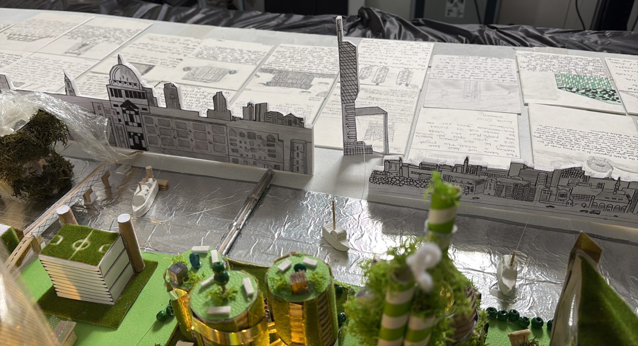 Close-up of Year 6 pupils’ reimagined London Southbank architectural model, showing the River Thames with miniature boats, bridges and detailed London skyline drawings. In the bottom right, we can see the rooftop gardens of the reimagined Tate Modern. The children's description cards are displayed behind the model.